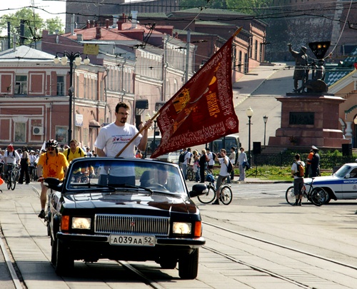 A replica of Kozma Minin 's banner is carried on a Volga convertible ahead of the bicycle of Valery Shantsev . May 2011, the "Minin's Road" cycling event