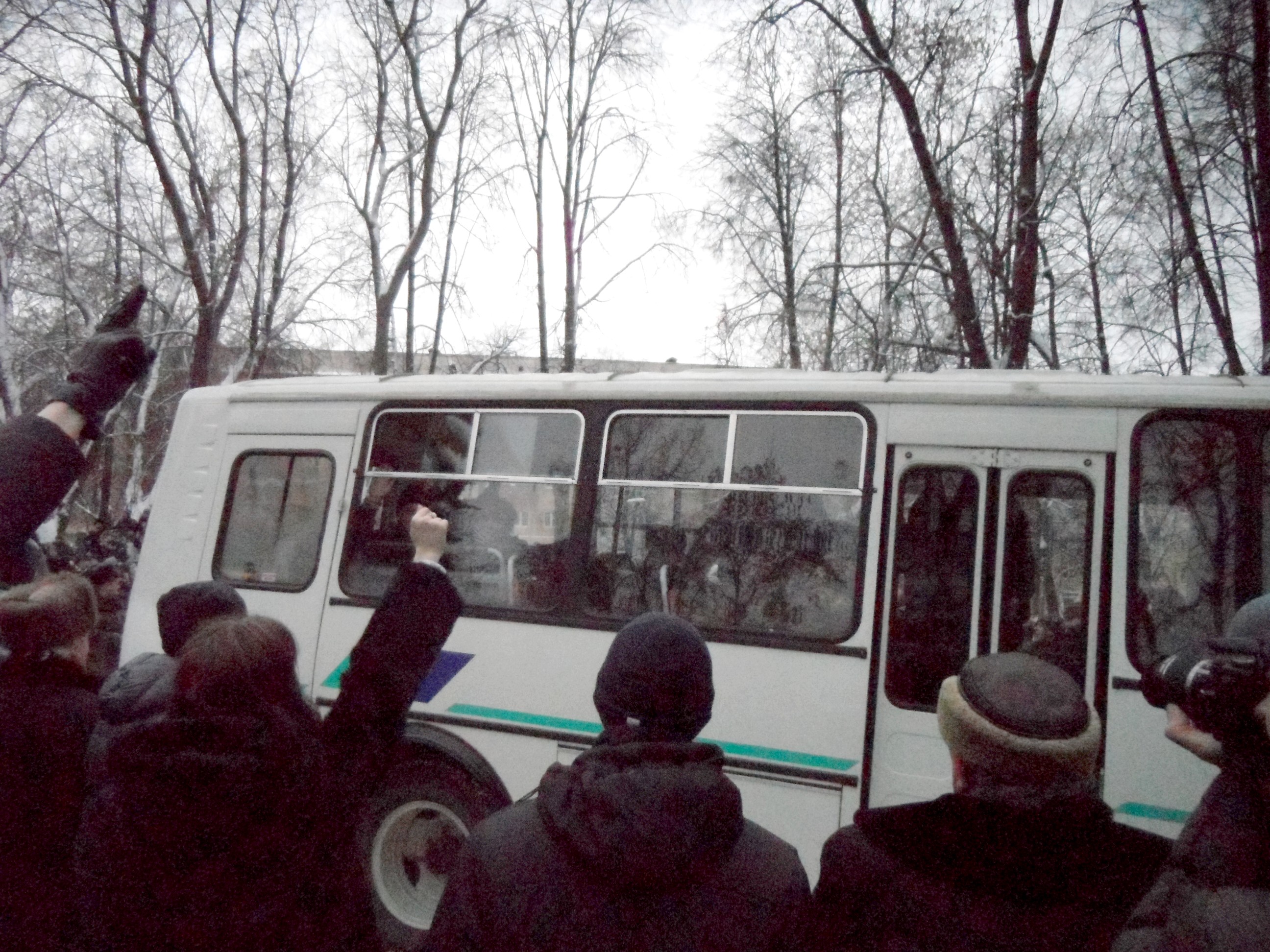 A demokrabus carrying detainees drives through the rally. Demonstrators greet the passengers with a raised clenched fist — the international symbol of civic solidarity