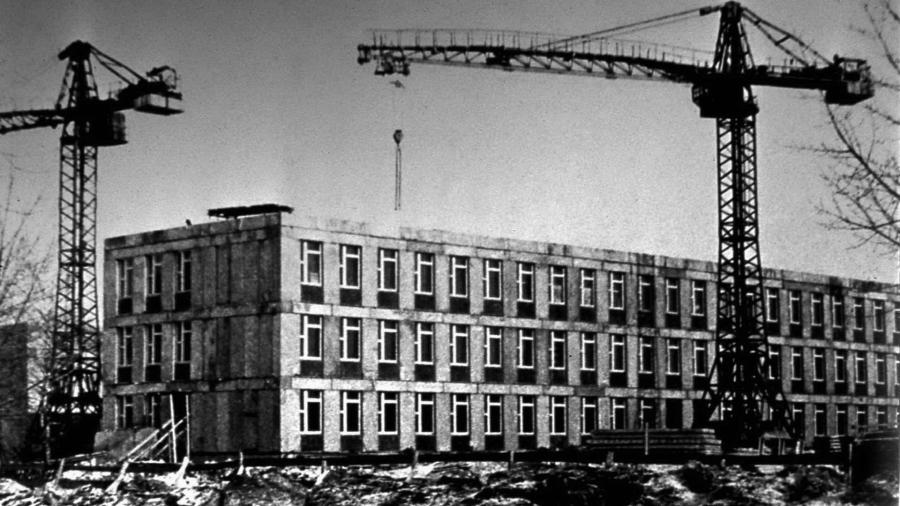 Construction of a four-storey building, two tower cranes on either side, winter wasteland